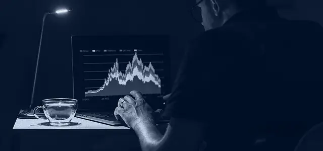 Man looking at abstract graph on a laptop with a light illuminating the background